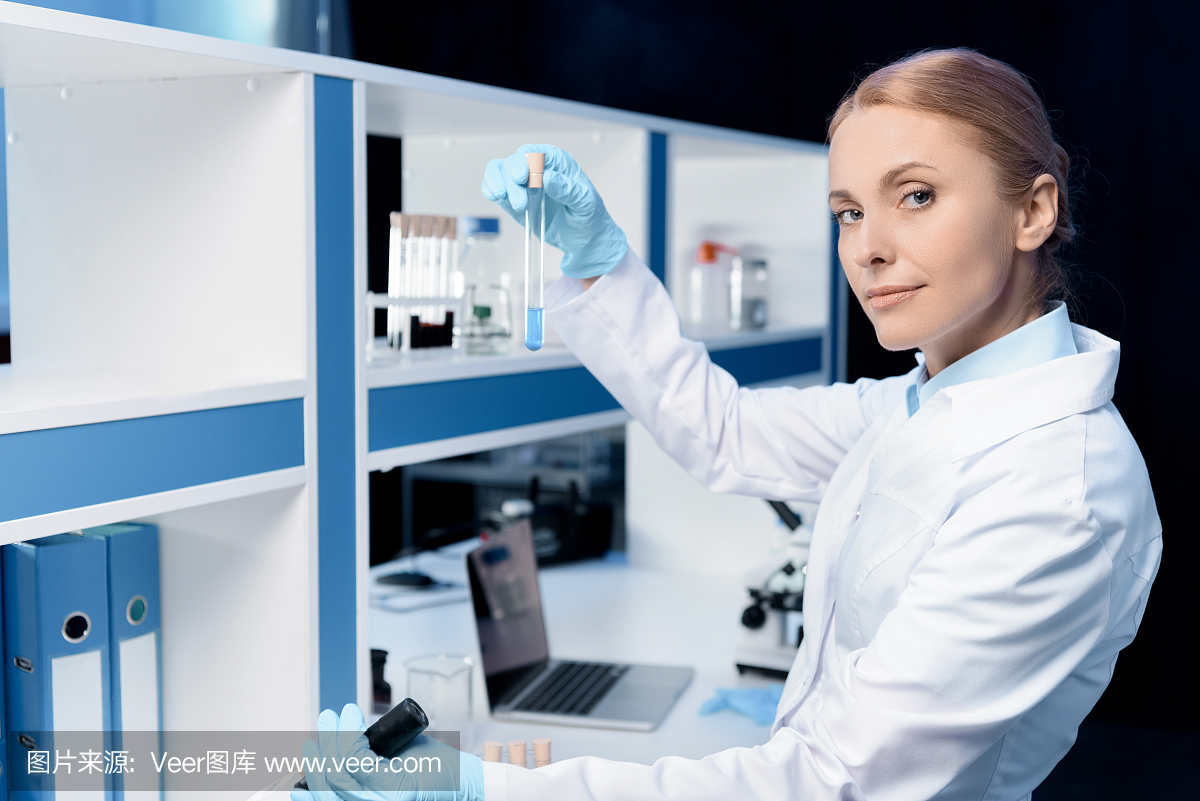 在实验室里,自信的科学家拿着带试剂的烧瓶,看着相机的侧视图
